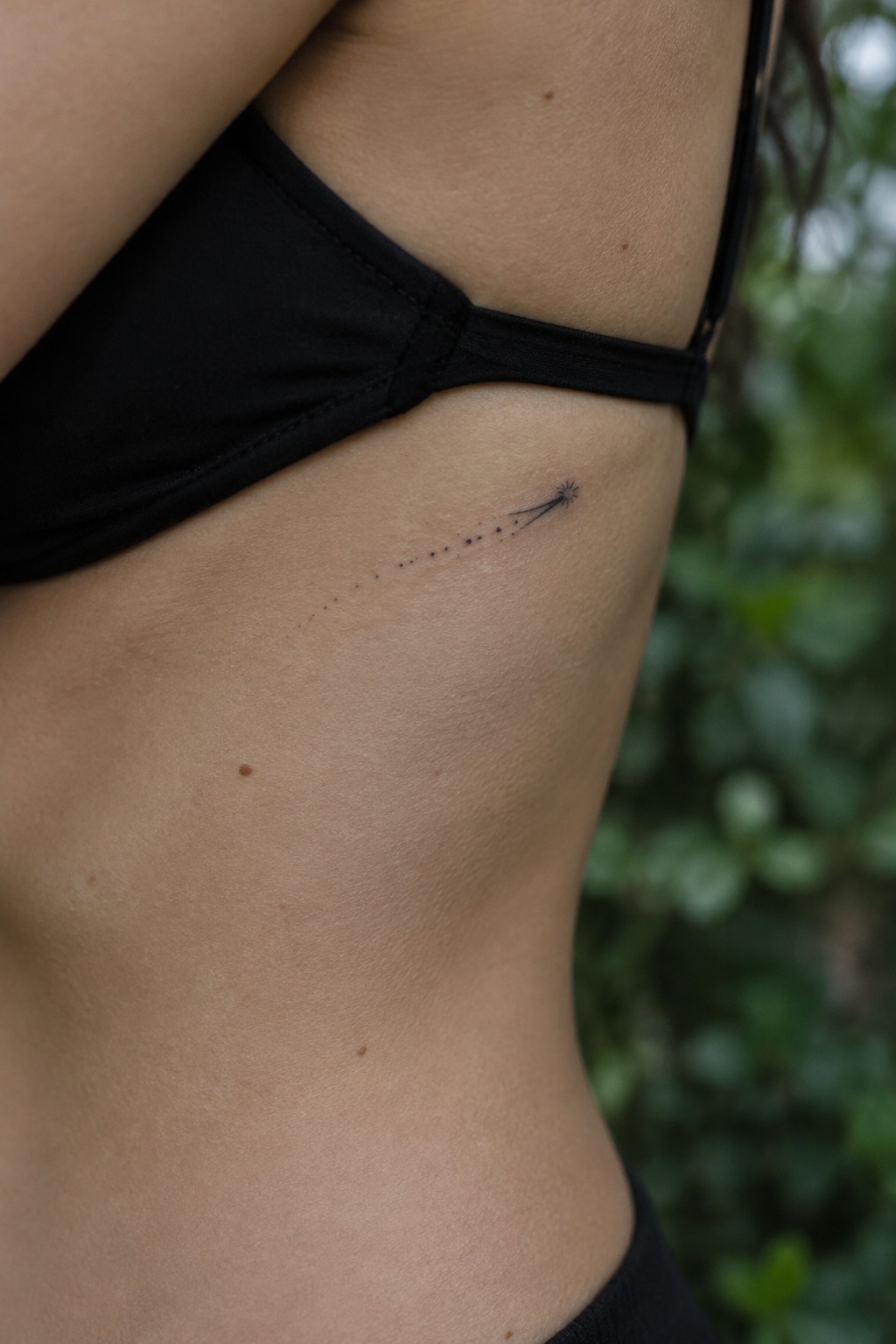 Small black shooting star tattoo on ribcage beside black bikini strap