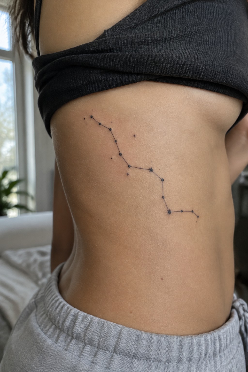 Constellation tattoo on midriff below black crop top and gray sweatpants