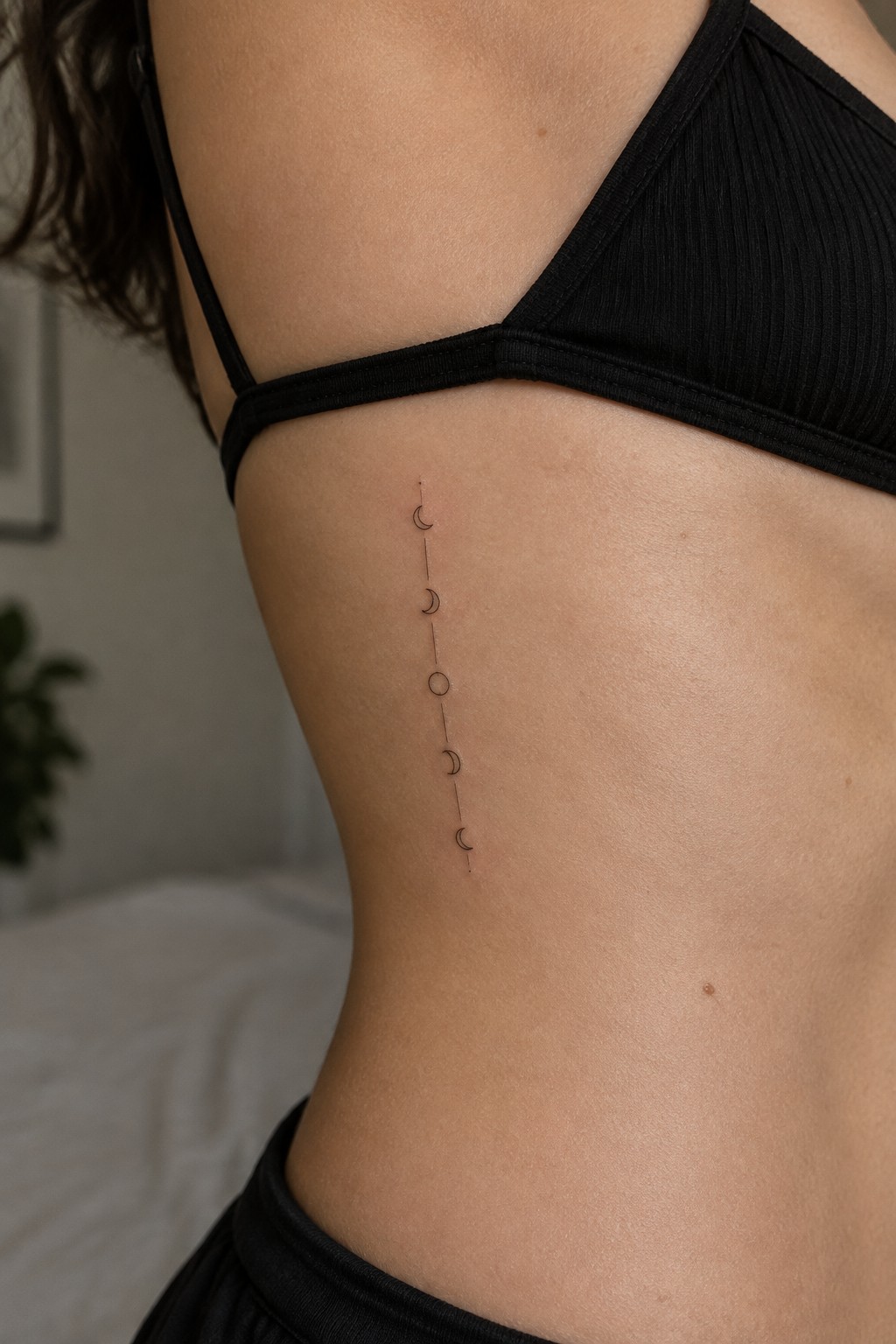 Moon phase tattoo vertically aligned on ribcage below black bralette