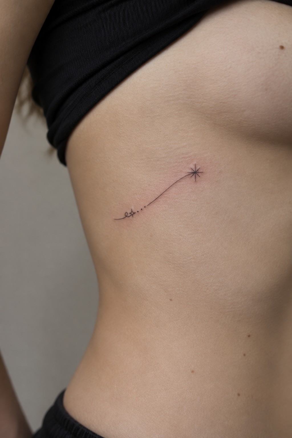 Minimalist shooting star tattoo on bare skin under black ribbed top
