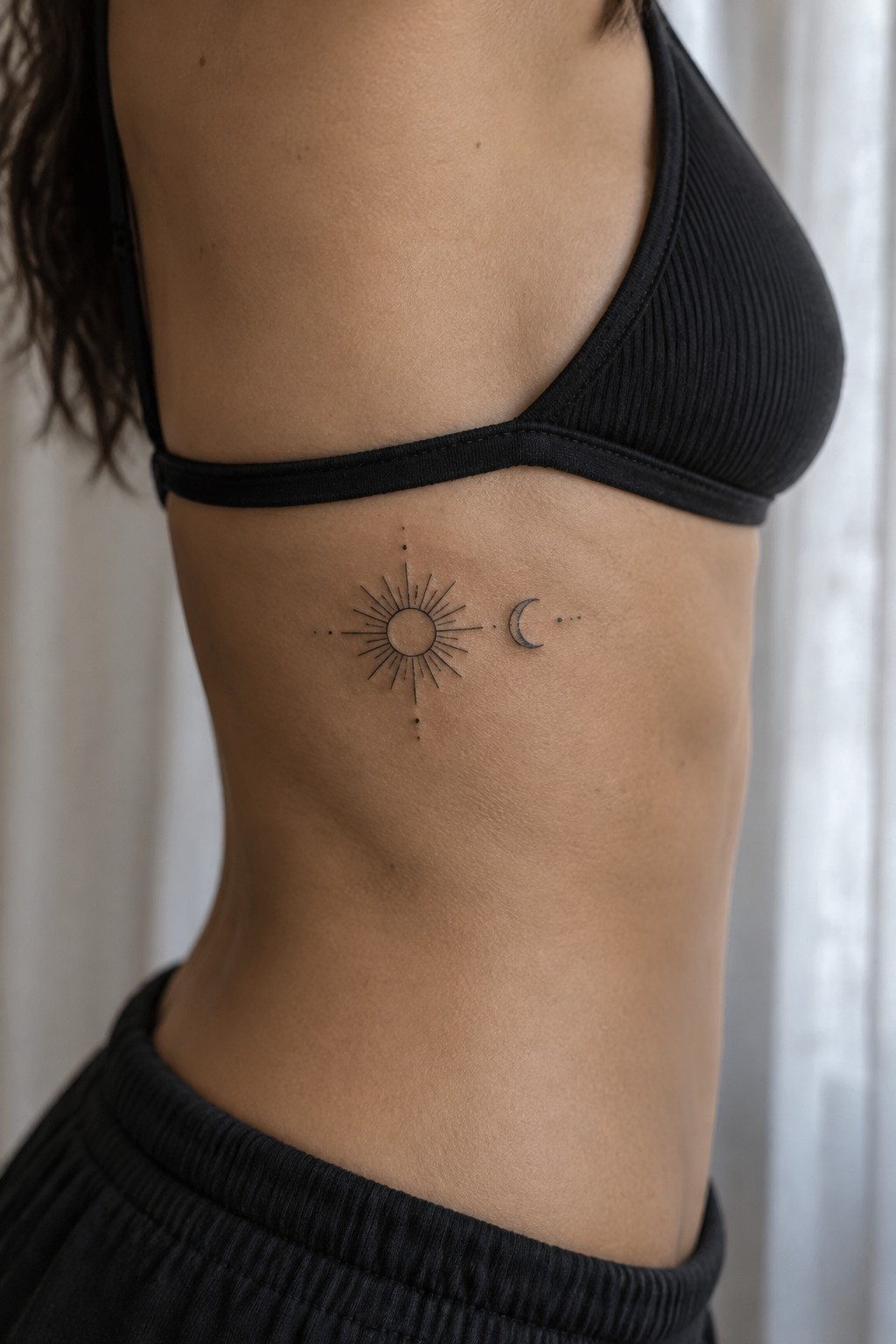 Minimalist fine line sun and moon tattoo placed horizontally on the ribs with small dots connecting the symbols.