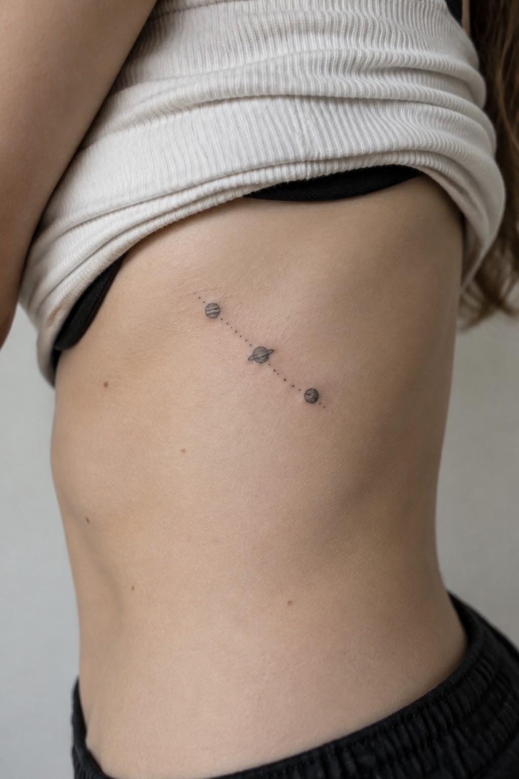 Minimalist tattoo of three planets linked by dots on torso under white shirt