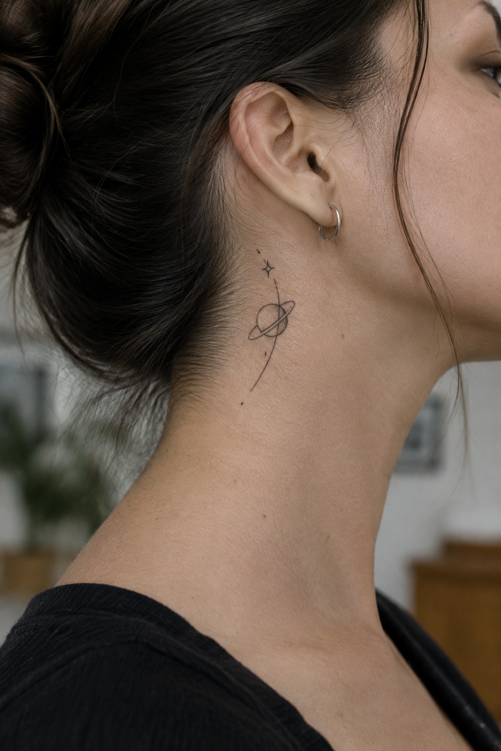 Woman's neck with minimalist ringed planet tattoo, dark bun, hoop earring