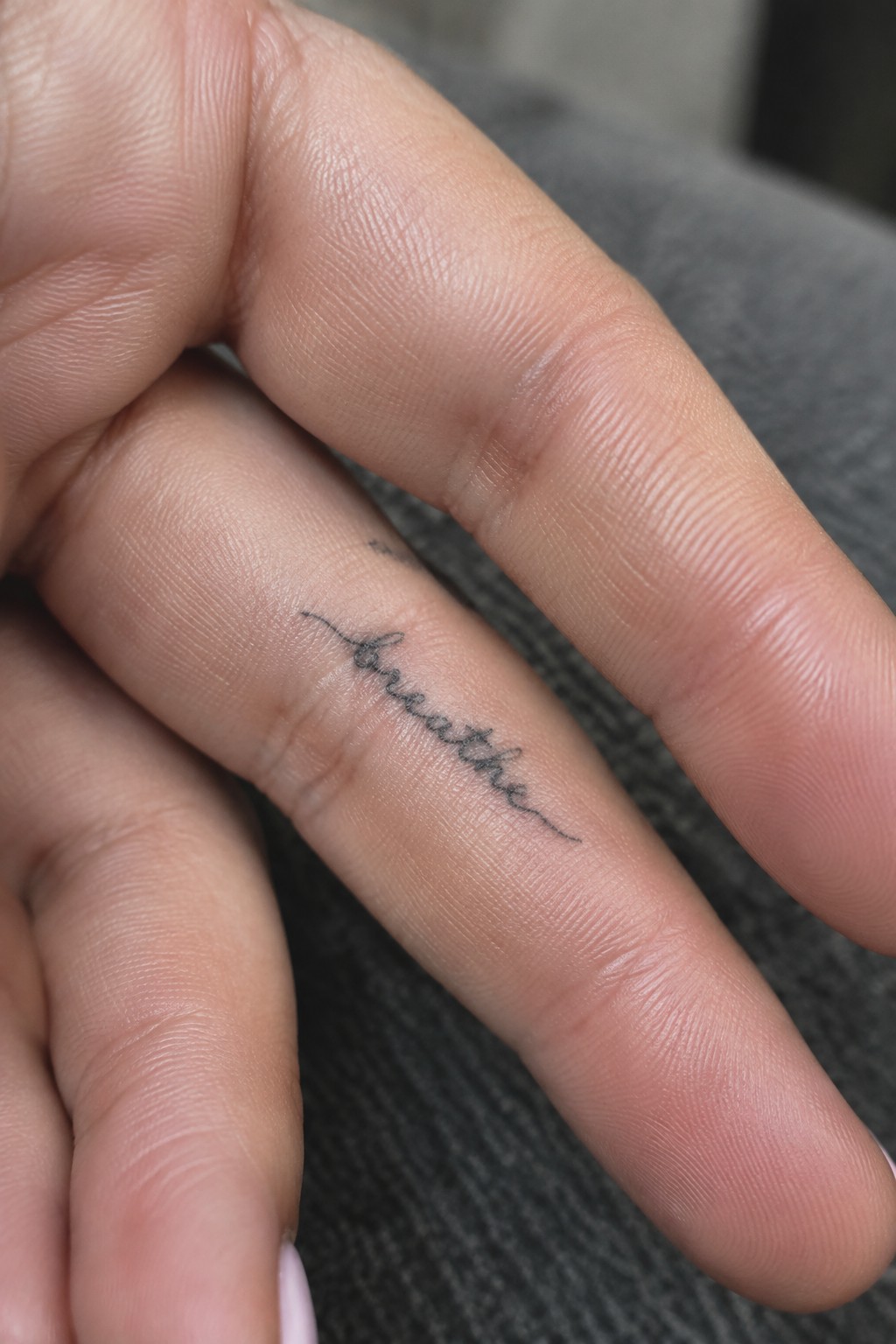 Single line script tattoo of the word breathe placed along the side of a finger