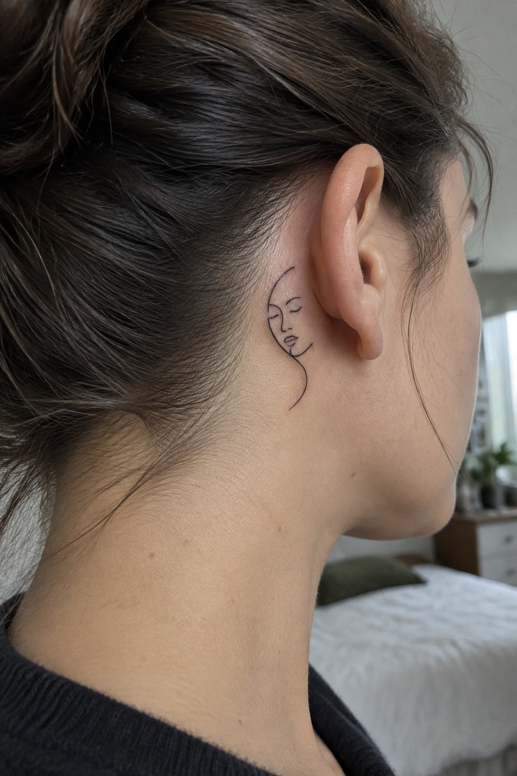 Woman with brown bun hairstyle and minimalist face line tattoo behind ear