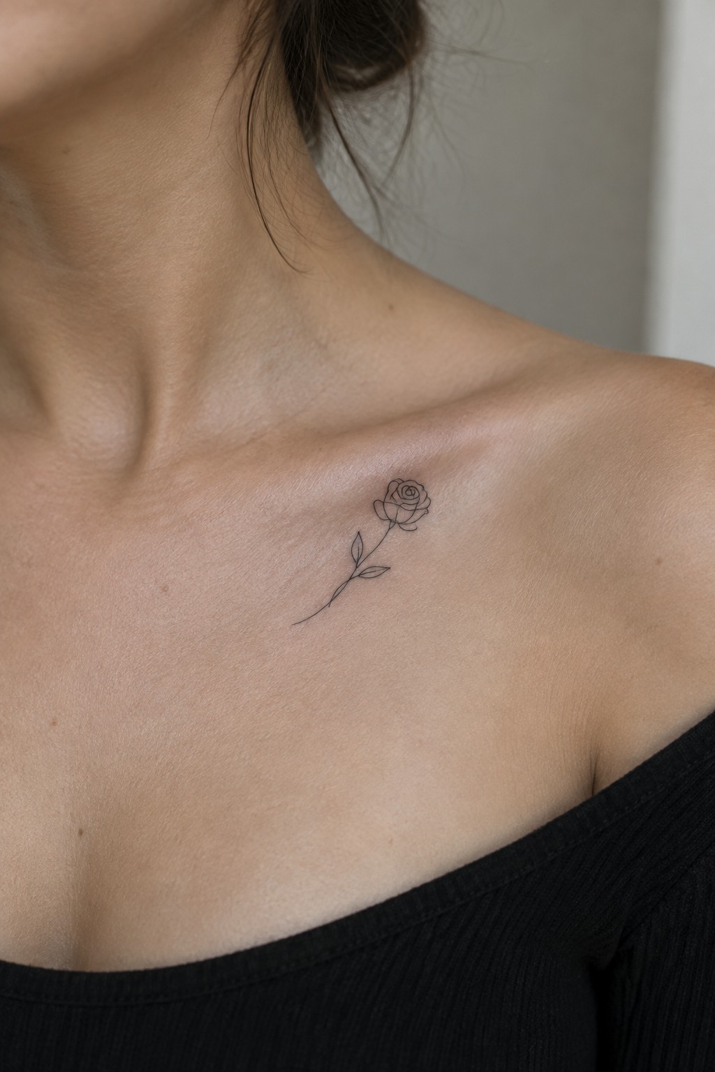 Minimalist rose tattoo on collarbone above black off-shoulder top