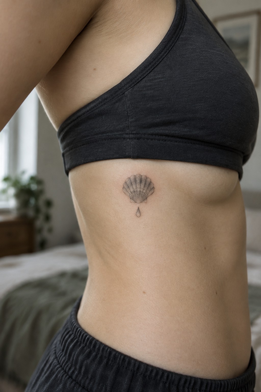 Fine line seashell tattoo with a small droplet below it on the side torso under the arm.