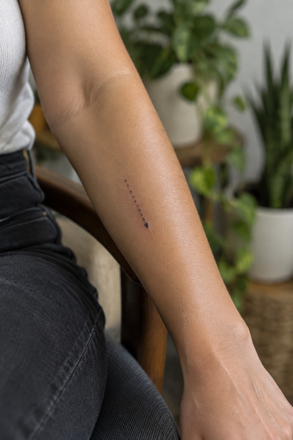 Forearm with dotted arrow tattoo, person in white shirt and dark jeans.