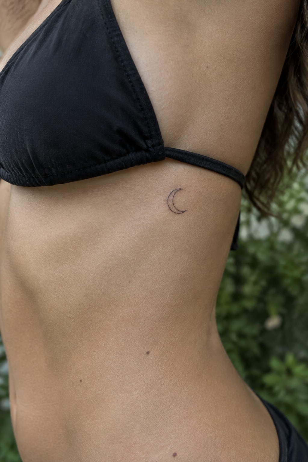 Black bikini top and small crescent moon tattoo on bare torso