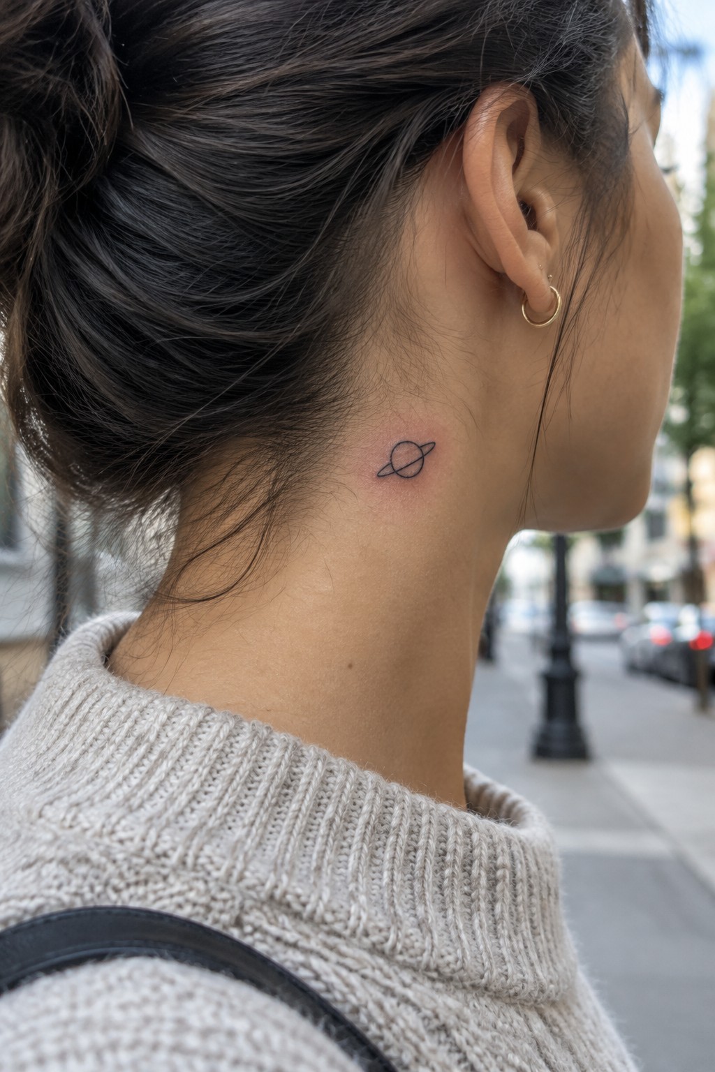 Woman with dark bun, planet tattoo on neck, beige knit sweater, gold earring