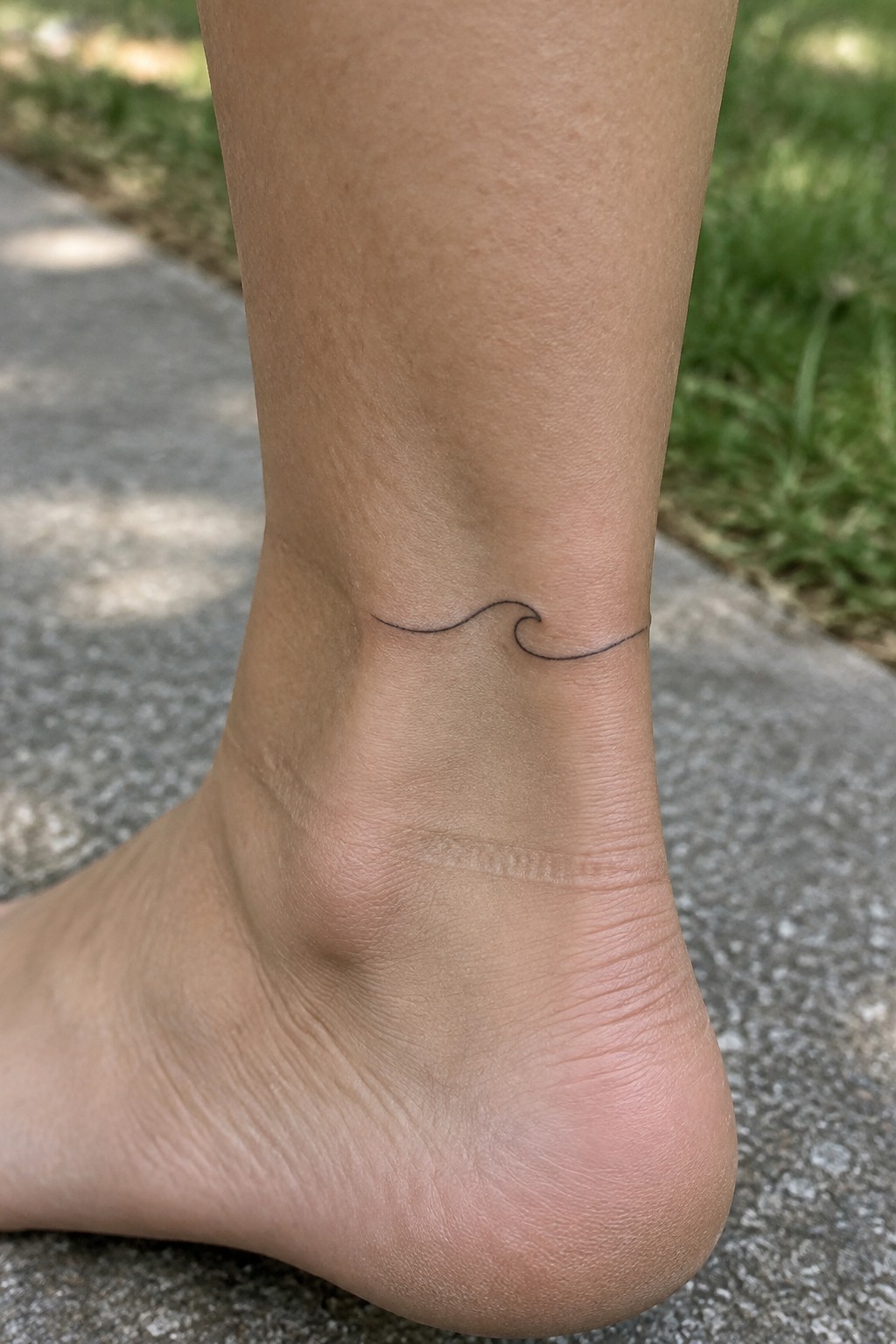 Small black wave tattoo on the outer side of an ankle.