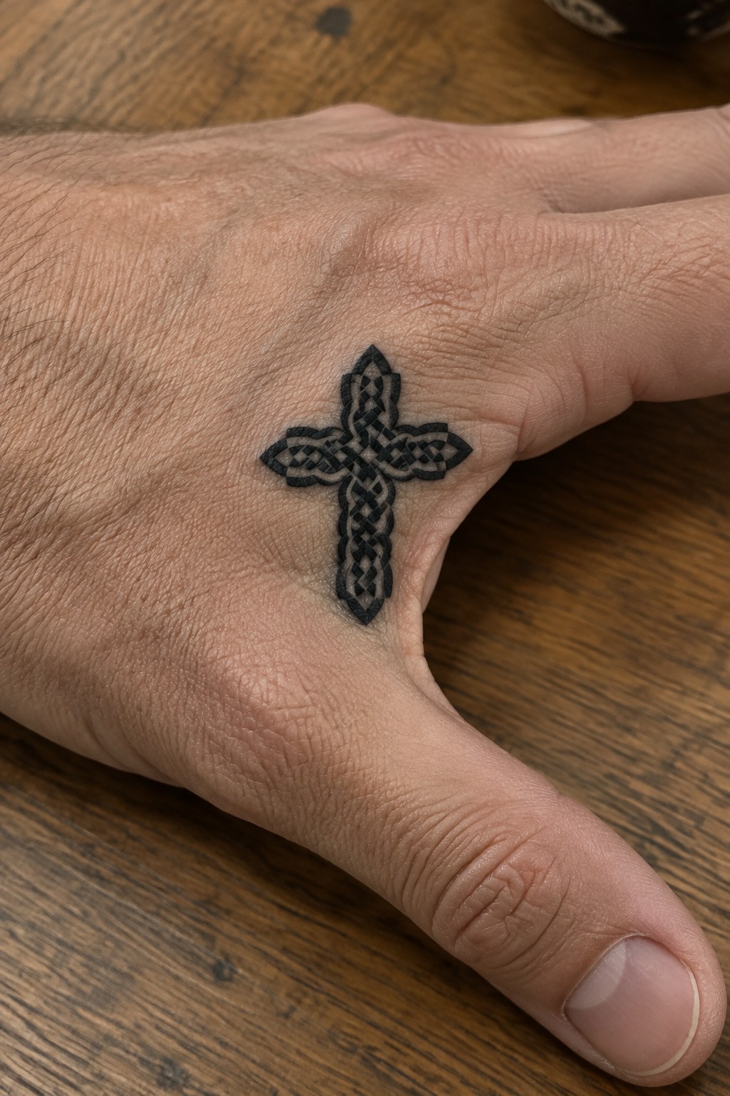 Black ink Celtic cross tattoo with knotwork patterns on the back of a hand.