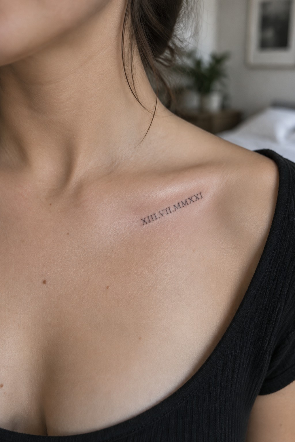 Fine-line Roman numeral date tattoo along a woman's collarbone above a black top.