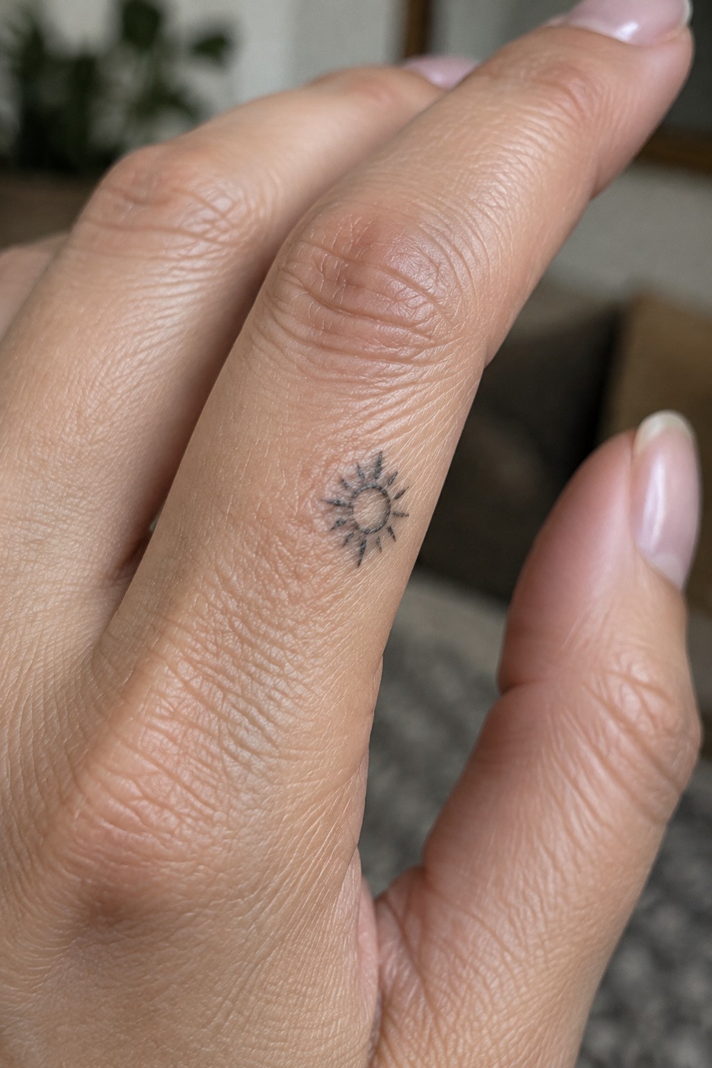 Small fine-line sun tattoo with a circular center and short rays on the side of a finger.