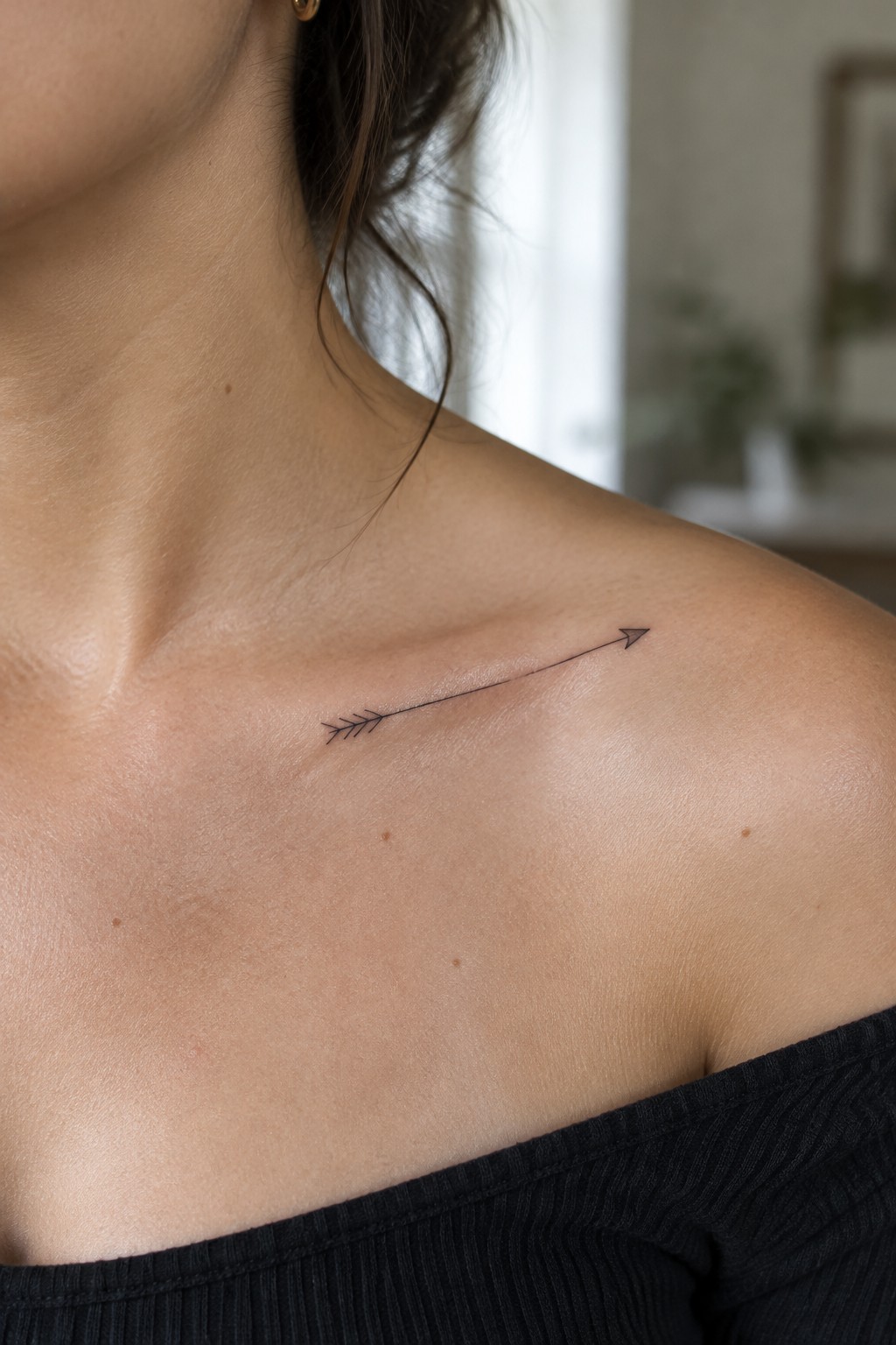 Fine-line black arrow tattoo running diagonally across a woman’s collarbone.