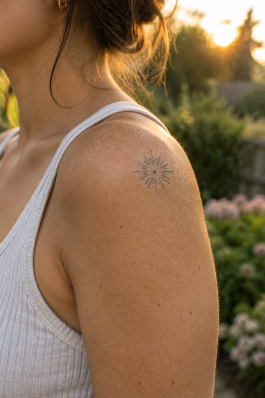 Small fine-line sunburst tattoo on a woman’s upper shoulder.