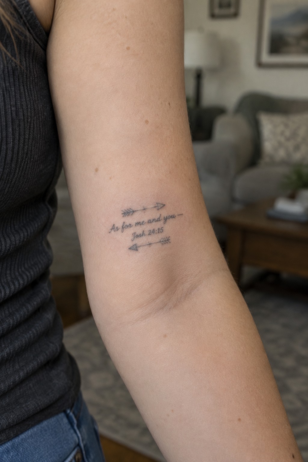 Inner forearm tattoo showing the verse As for me and you from Joshua 24:15 placed between two small arrow symbols.