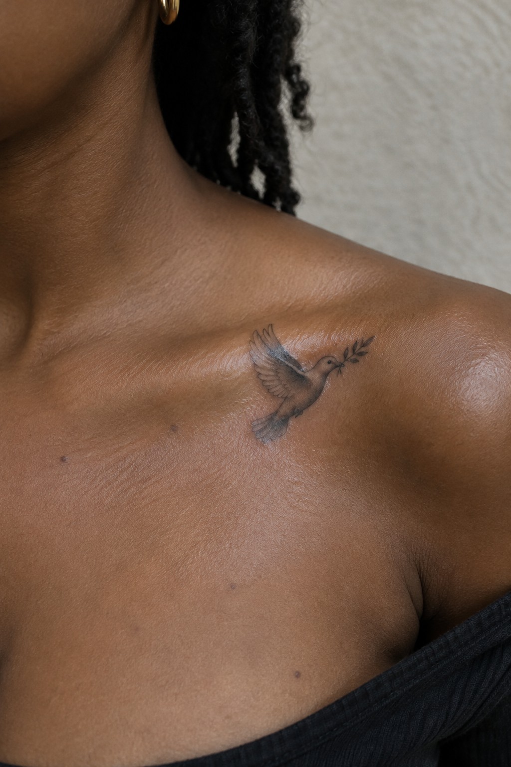 Flying dove with olive branch tattoo on dark-skinned collarbone.
