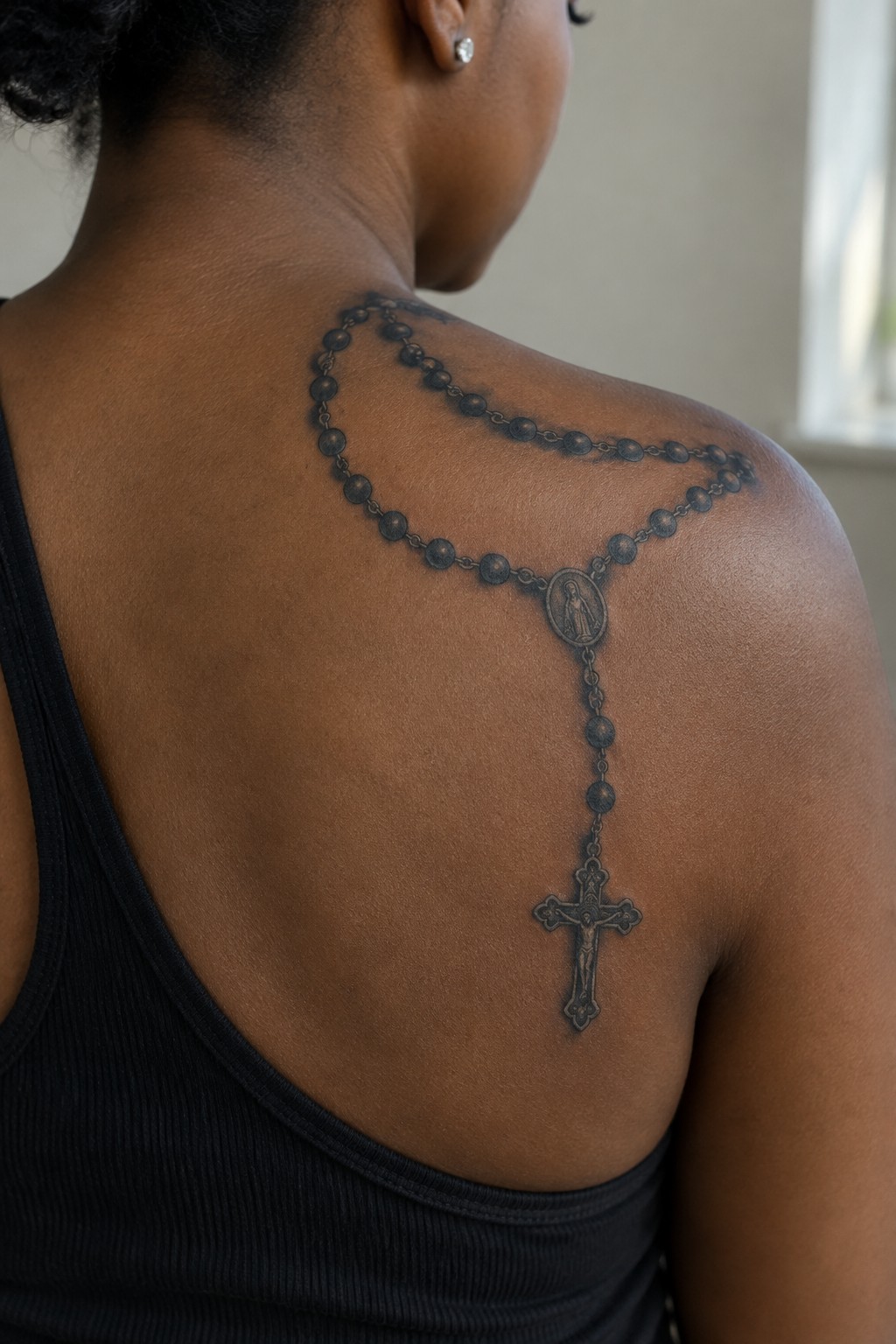 Rosary bead tattoo with crucifix on back of person in black tank top