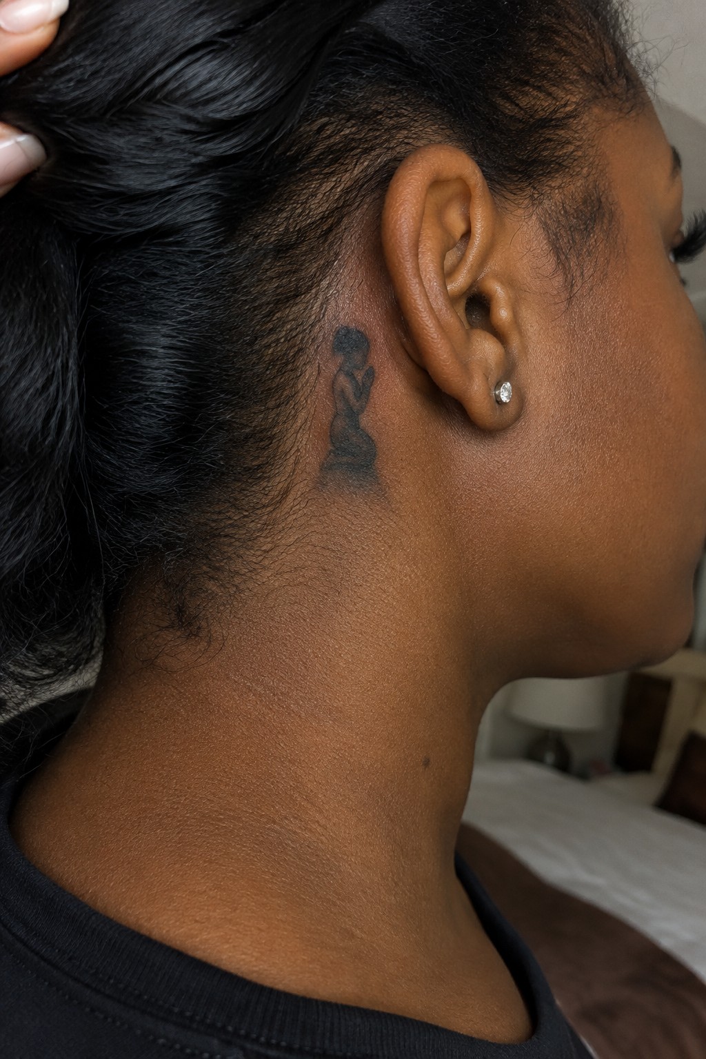 Black woman with pulled-back hair, small tattoo behind ear, diamond stud earring