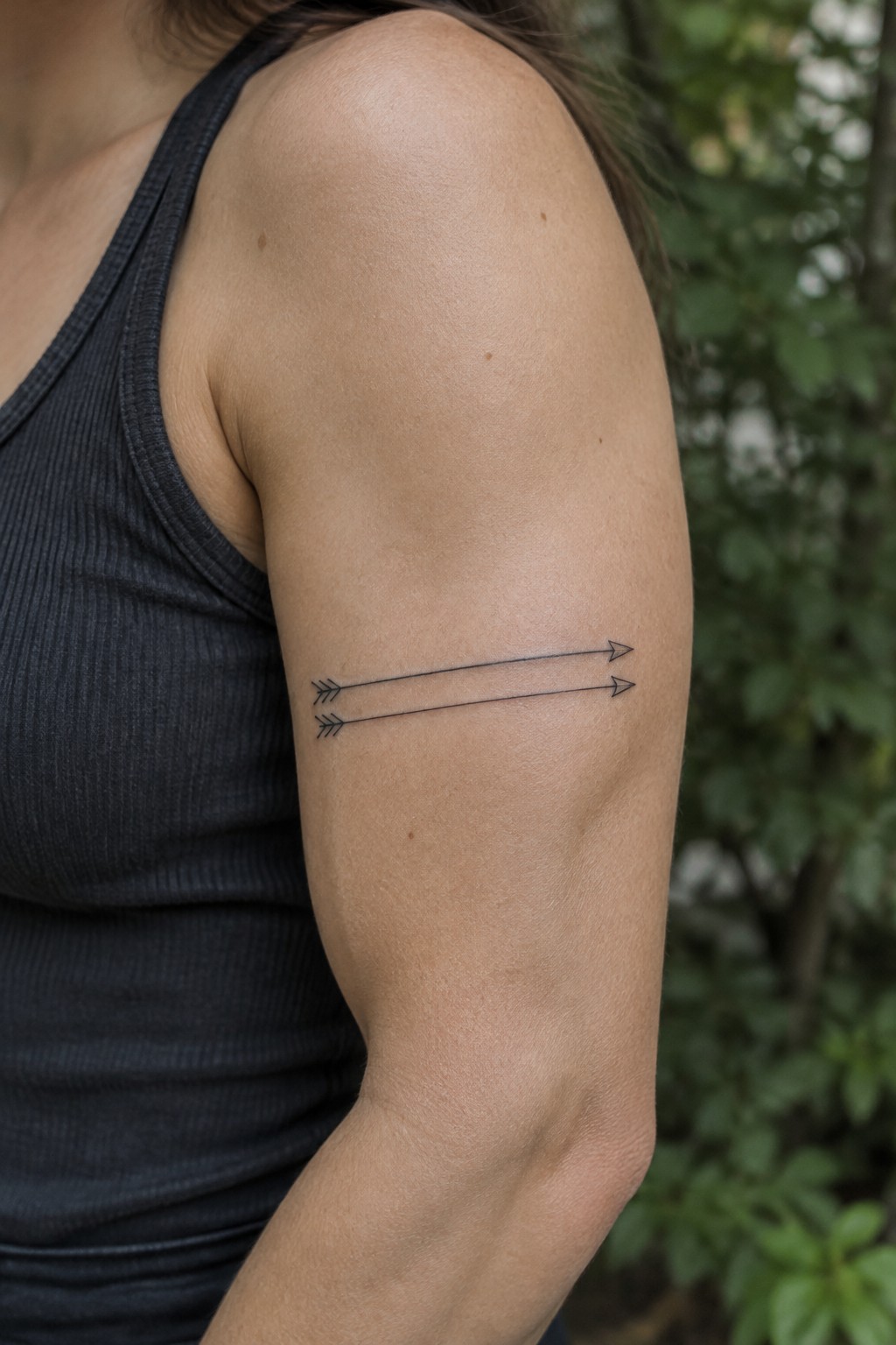 Two small, parallel fine-line arrows tattooed horizontally on the outer upper arm.