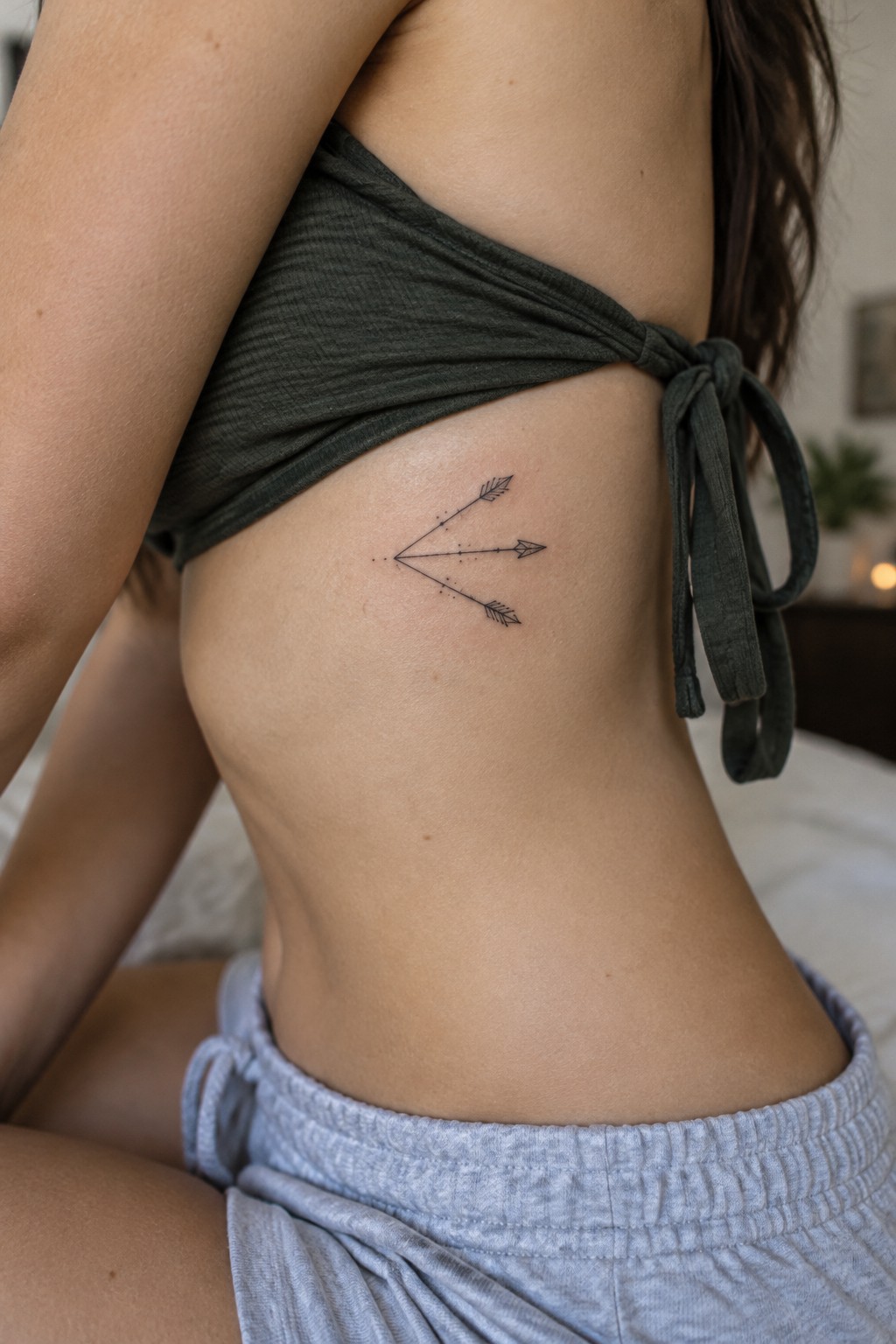 Small fine-line tattoo of three arrows pointing in different directions on a woman’s side ribs.