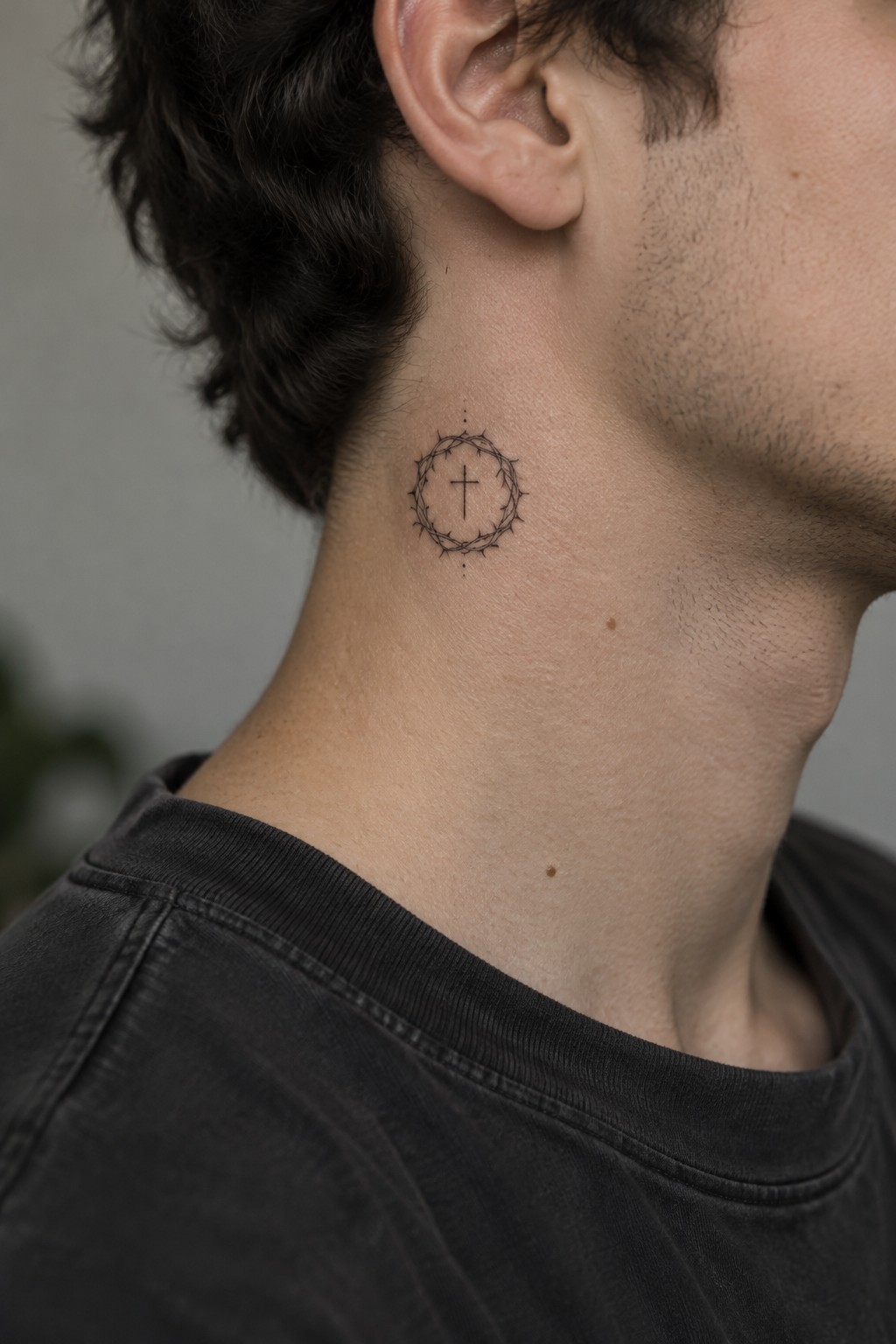 Man's neck with black crown of thorns and cross tattoo below ear