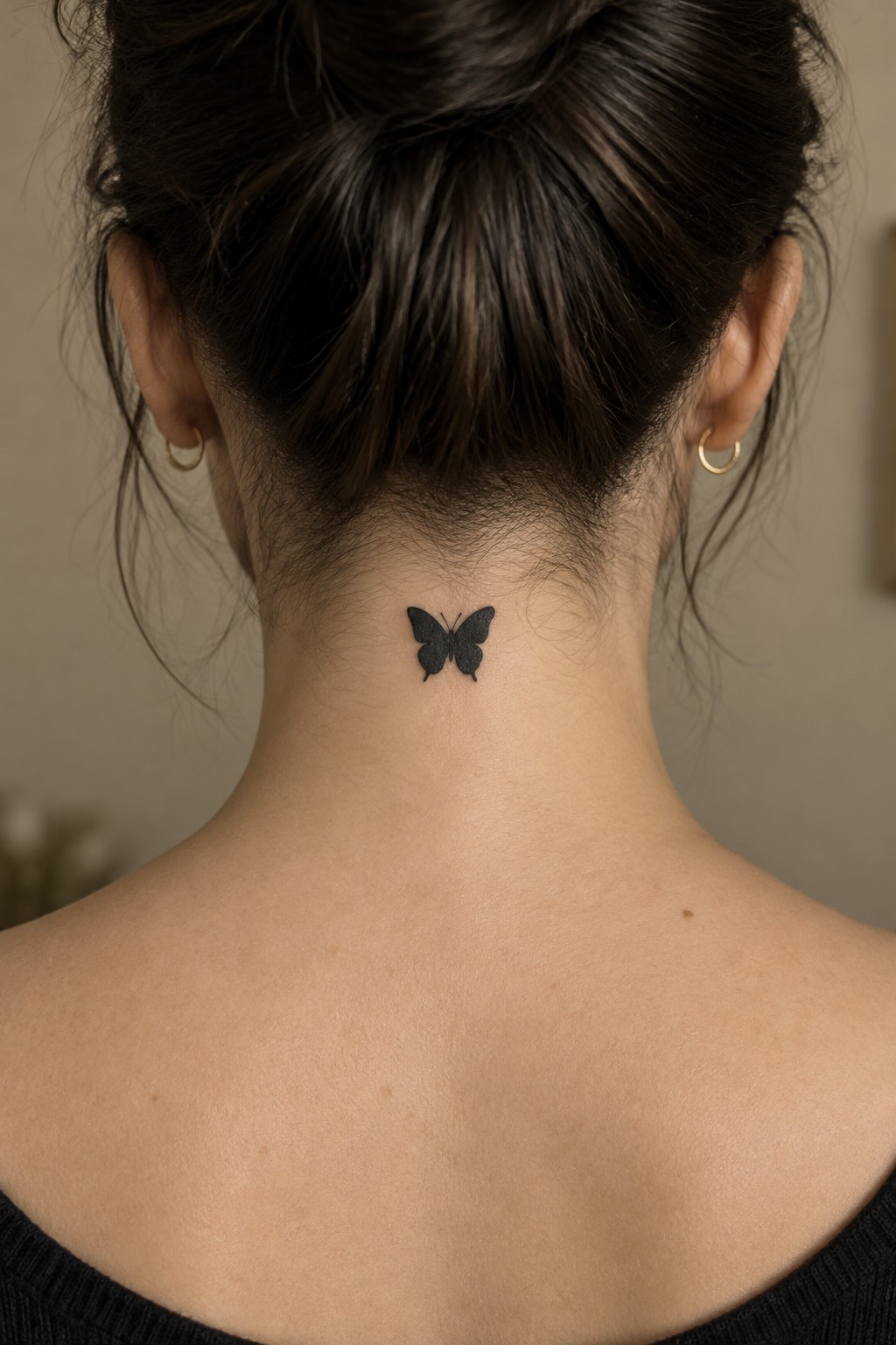 Small black butterfly tattoo centered at the nape of a woman’s neck, below her updo.
