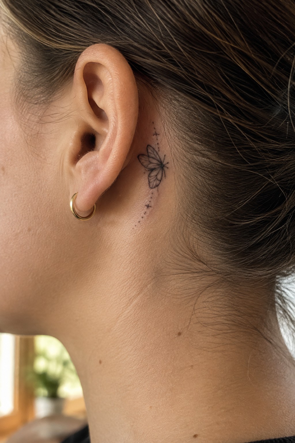 Small fine-line butterfly tattoo with a dotted trail and tiny stars behind a woman’s ear.