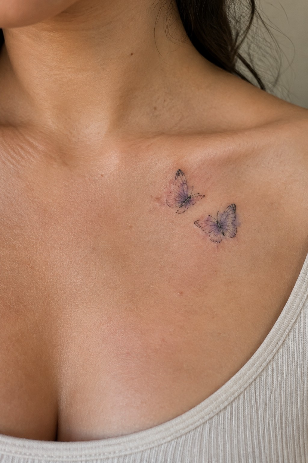 Two small fine-line butterflies with muted color tattooed near the collarbone.