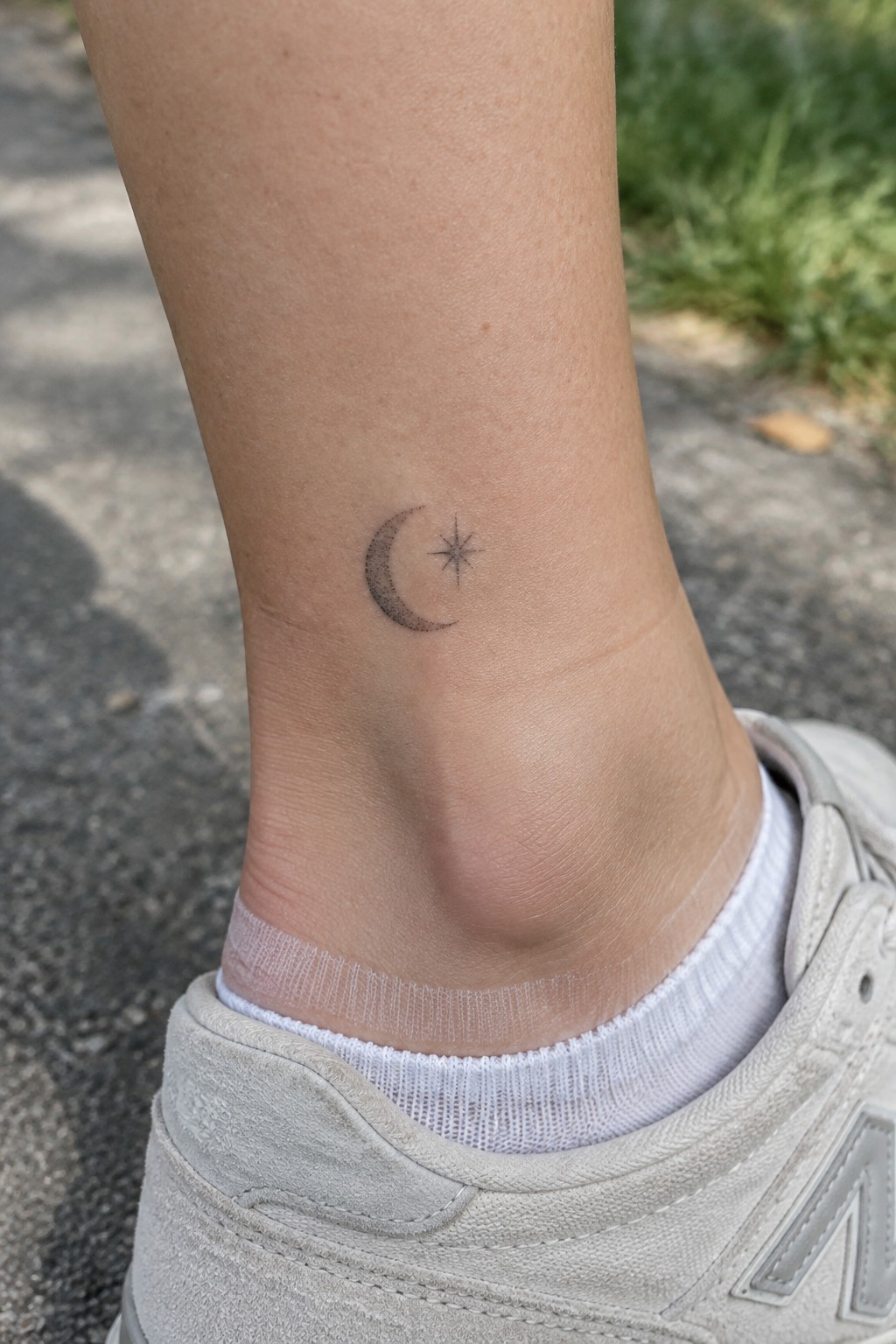 Small black crescent moon and star tattoo above the ankle, just above a white sock and sneaker.
