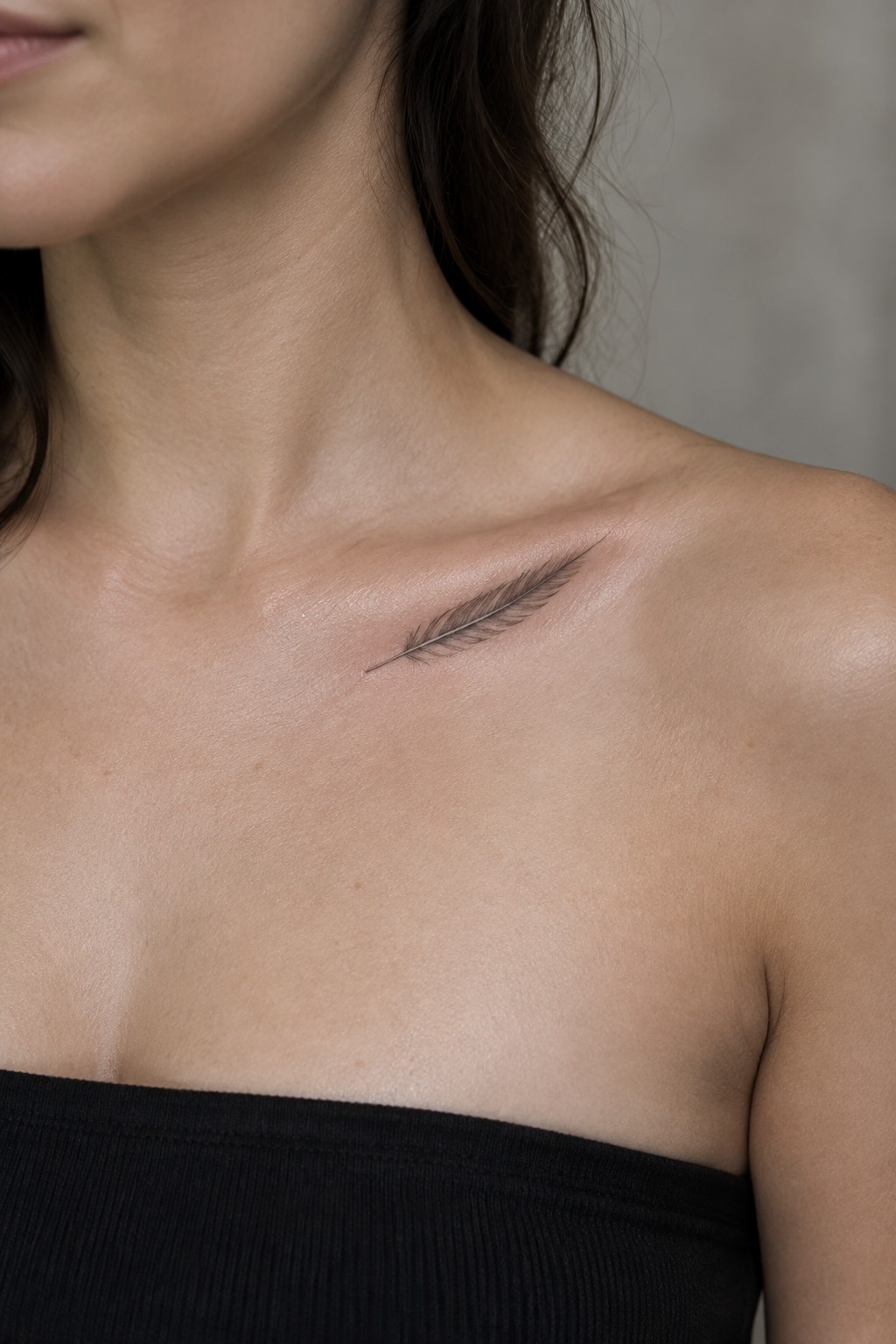 Small fine-line feather tattoo placed along a woman’s collarbone.