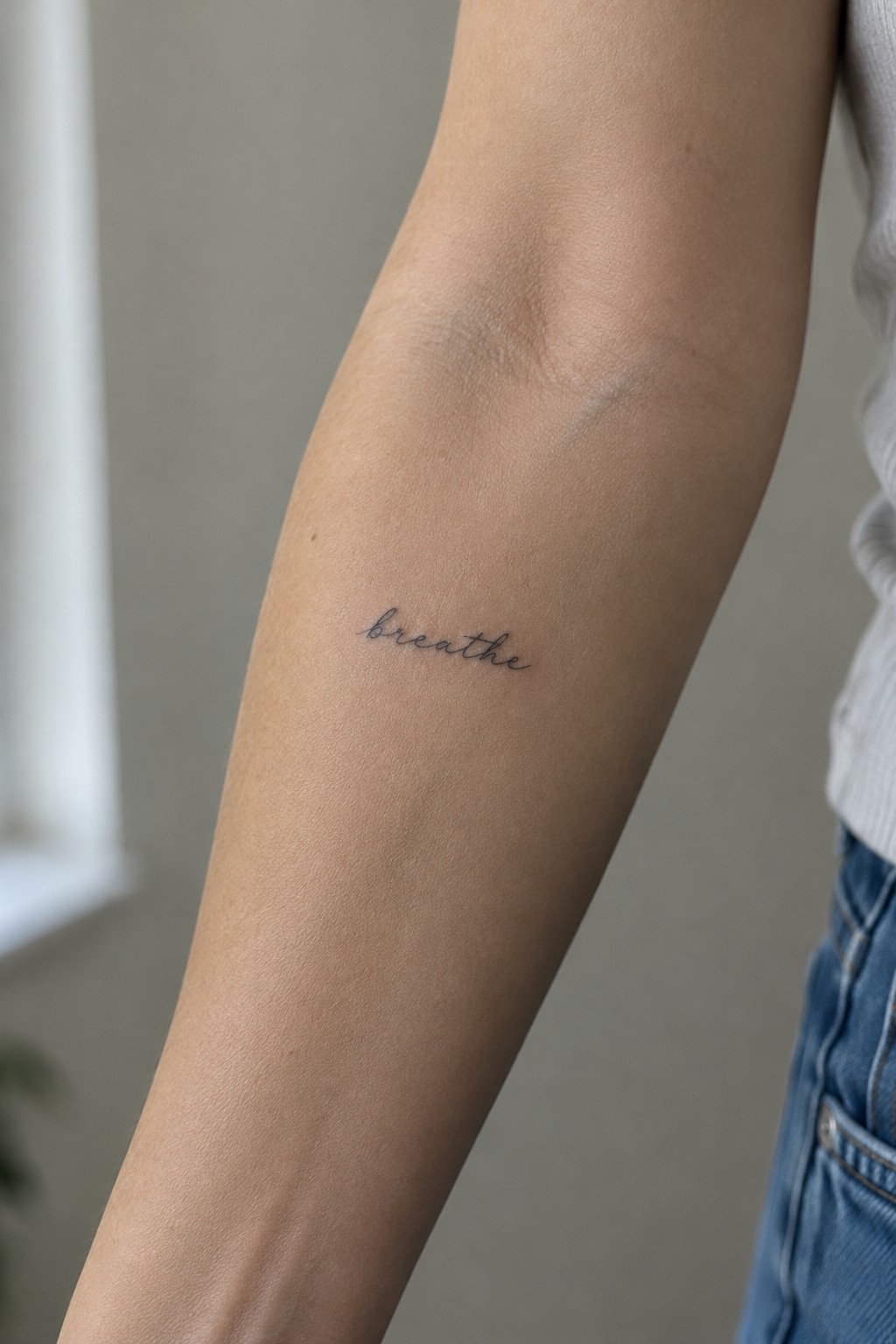 Small cursive “breathe” tattoo on the inner arm below the elbow.
