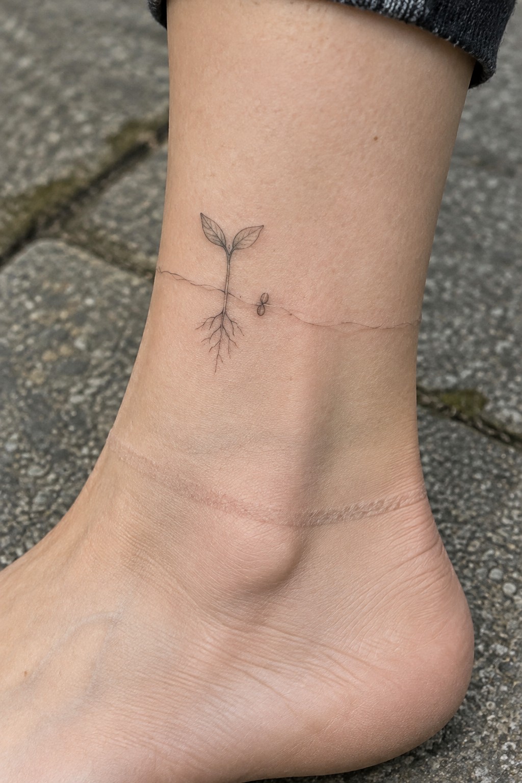 Black ink plant sprout tattoo with roots on ankle above bare foot