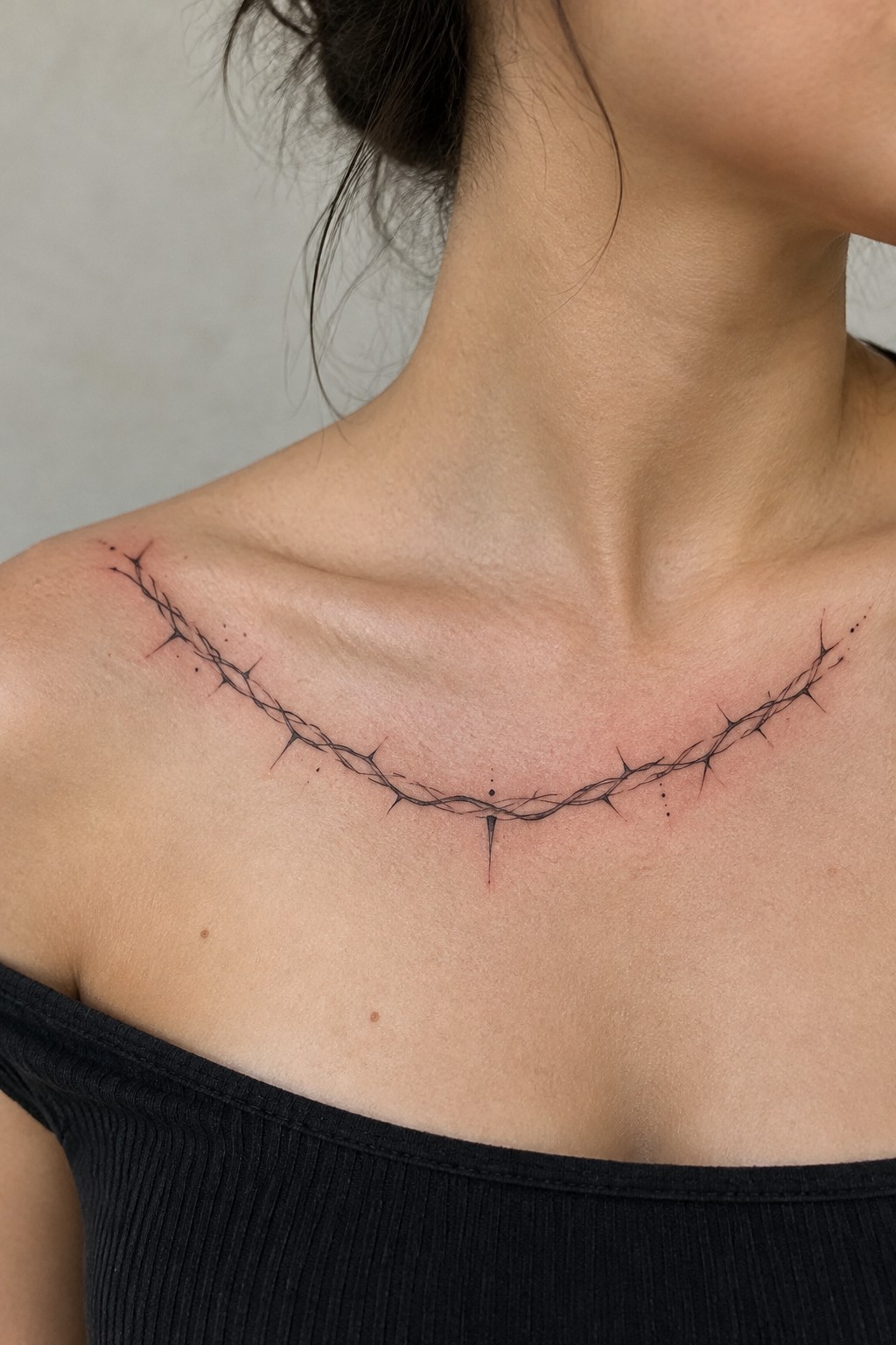 Barbed wire tattoo across collarbones above black off-shoulder top