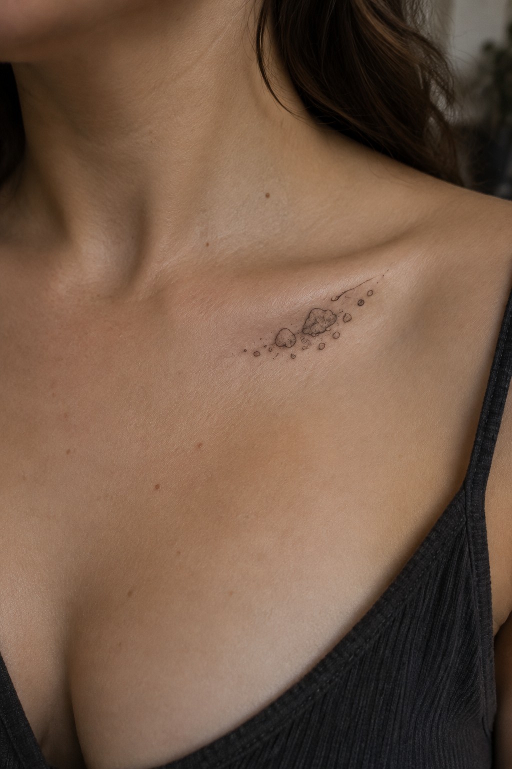 Woman's collarbone with small asteroid tattoo above dark gray tank top neckline