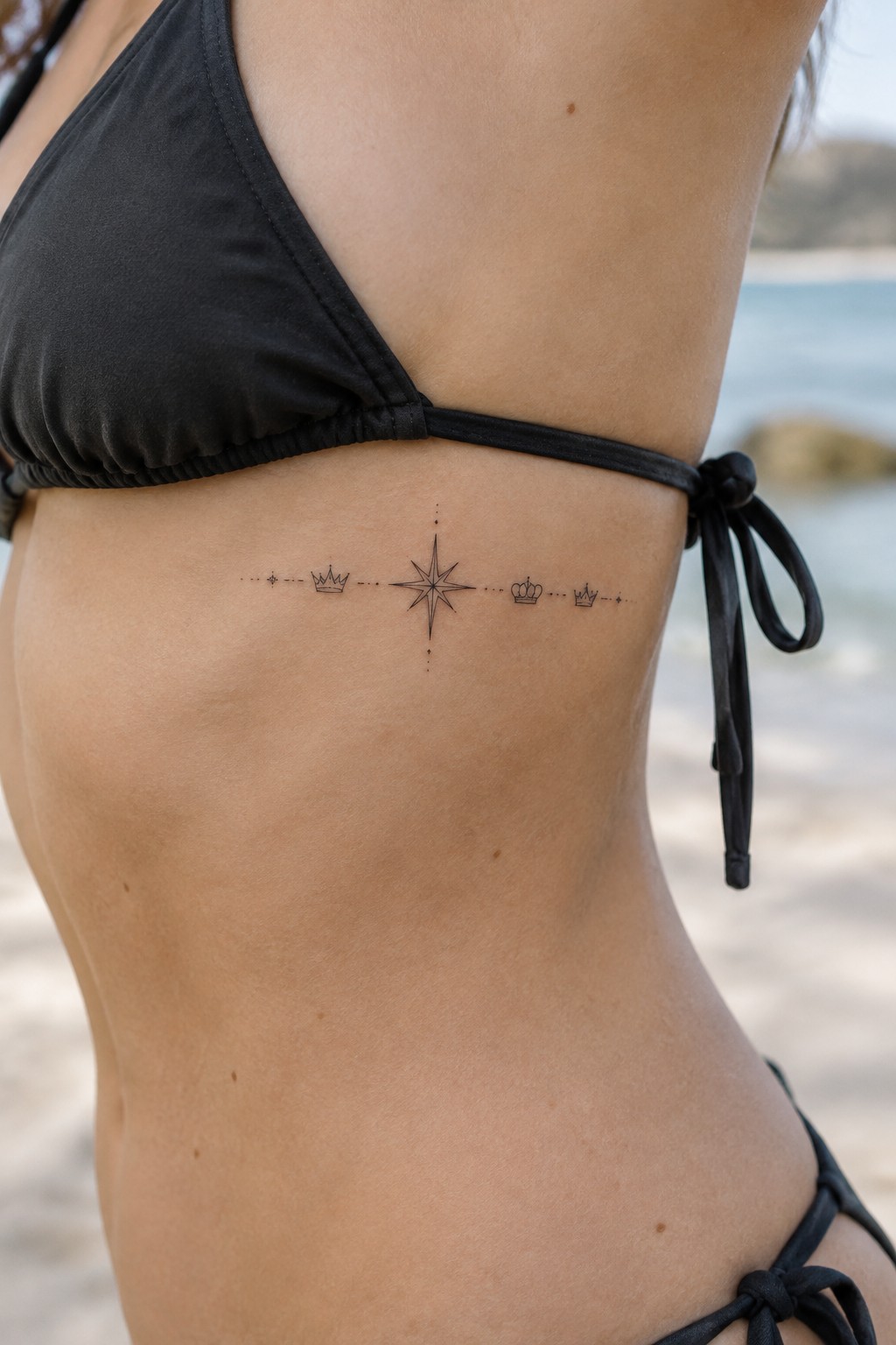 Woman in black bikini with compass rose and crown tattoo on ribs at beach