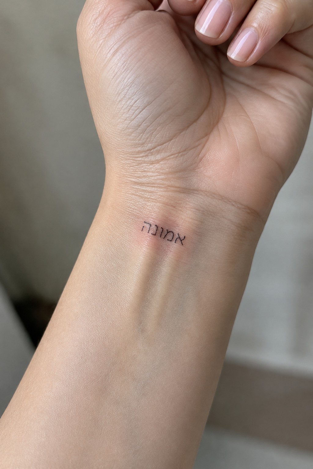 Wrist close-up with black Hebrew tattoo beside red mark and manicured pink nails
