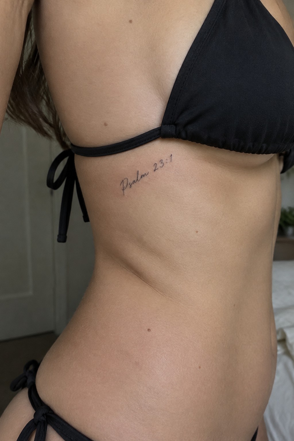 Torso in black bikini with Psalm 23:1 tattoo on ribcage