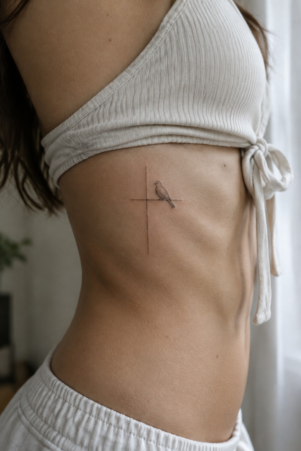 Bird tattoo on cross across ribcage below white tied crop top