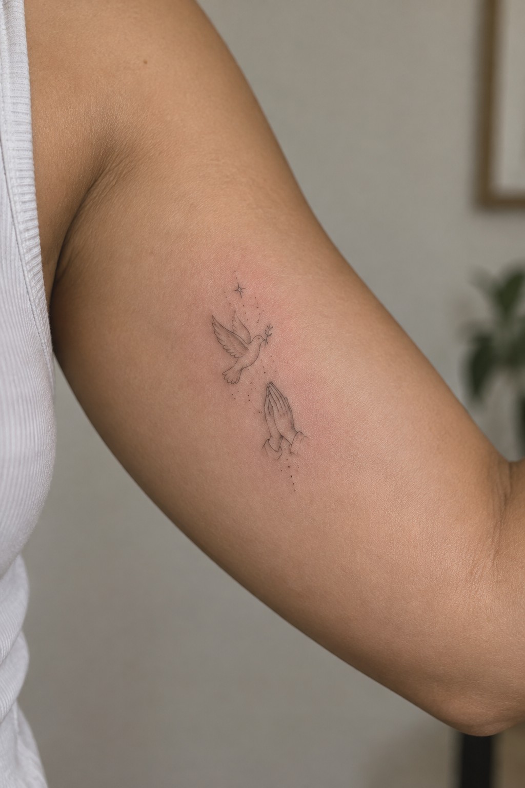 Fine line tattoo of flying dove and praying hands on upper arm
