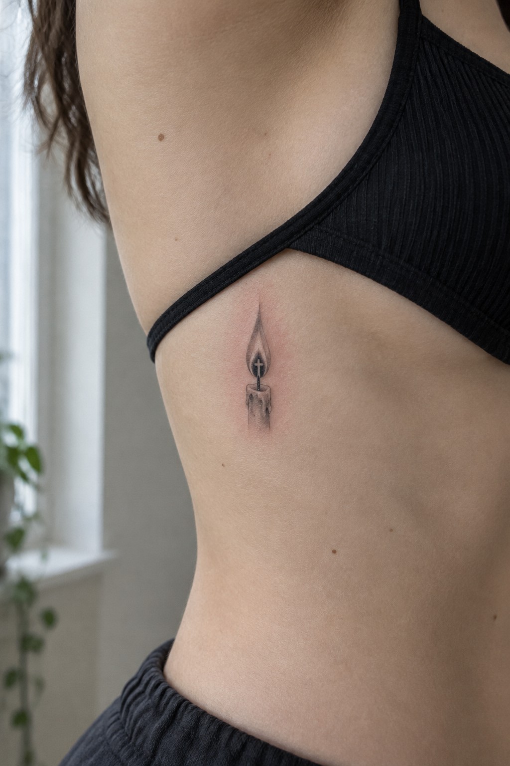 Small shaded candle tattoo on a woman's side beneath the edge of a black top.