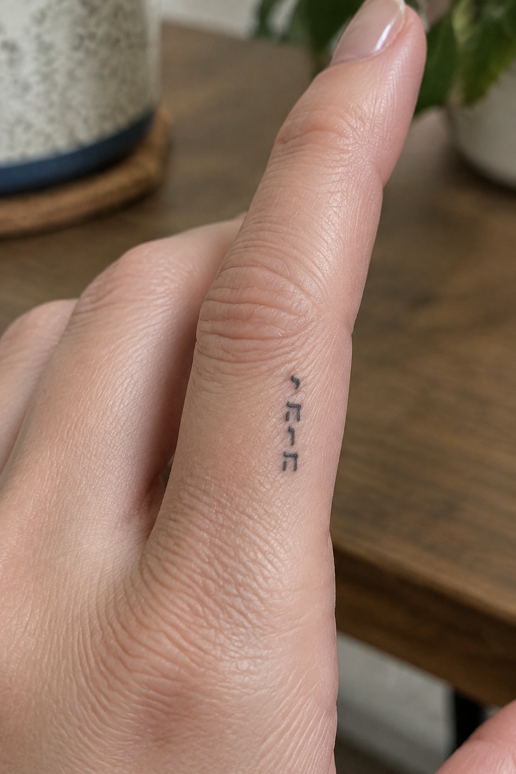 Finger with vertical black FREE tattoo on blurred wooden table background