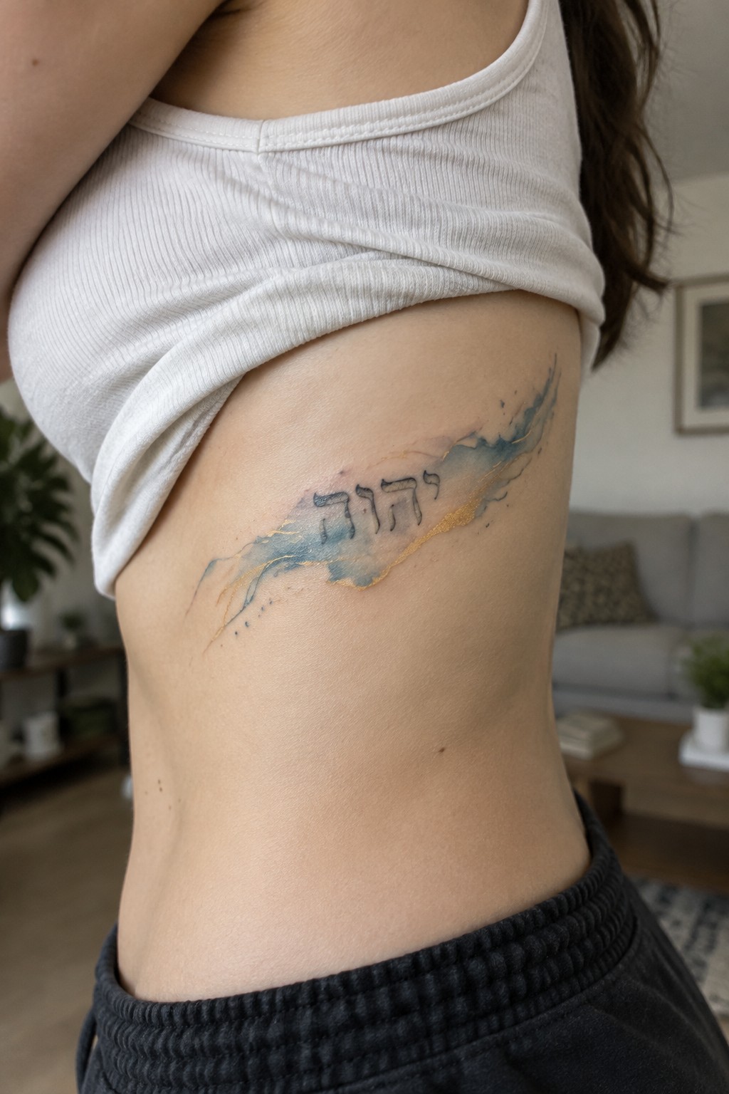 Hebrew tattoo with blue and gold watercolor on exposed side torso under white crop top