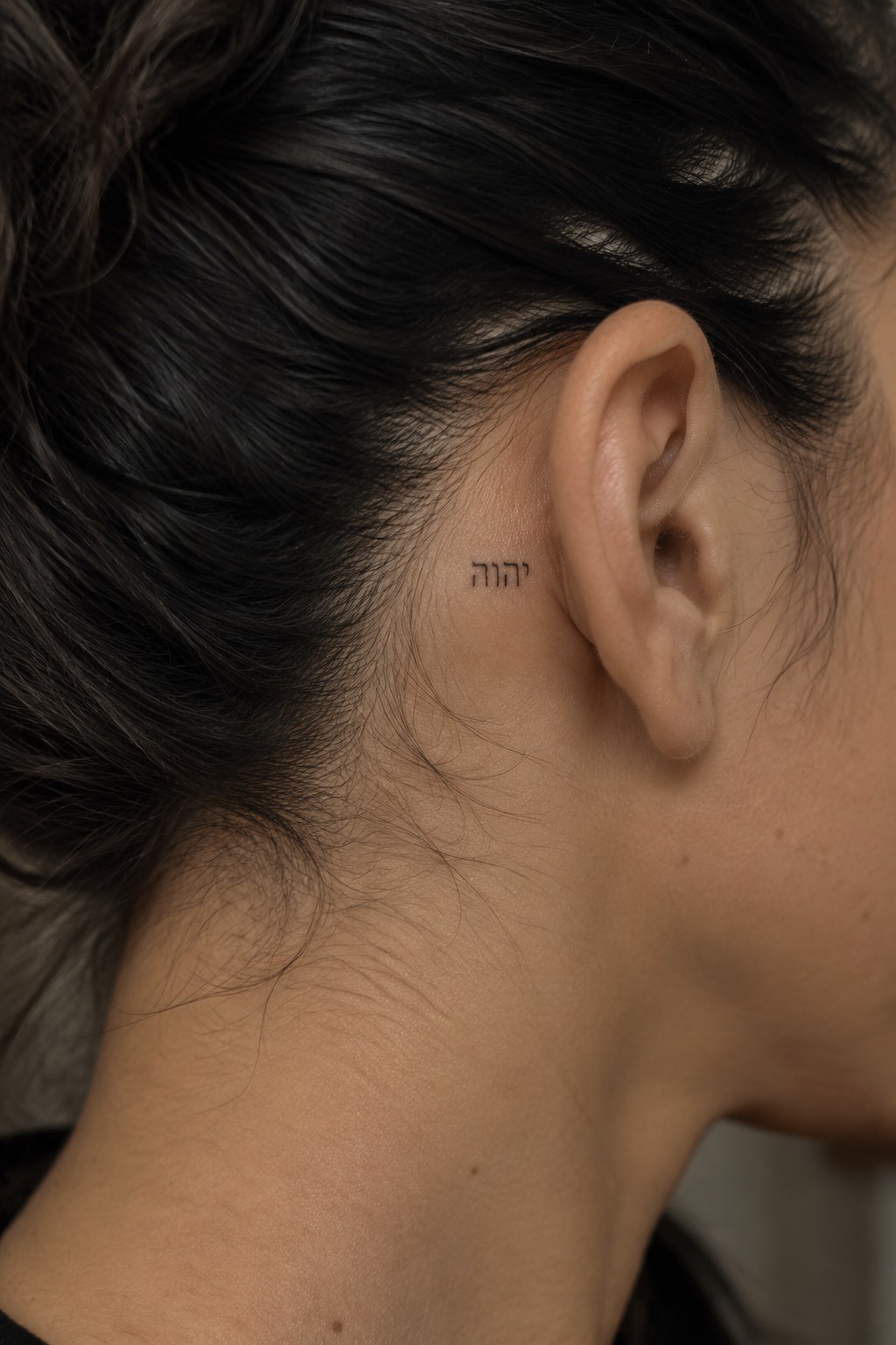 Small Hebrew tattoo behind ear on dark-haired person's neck and hairline