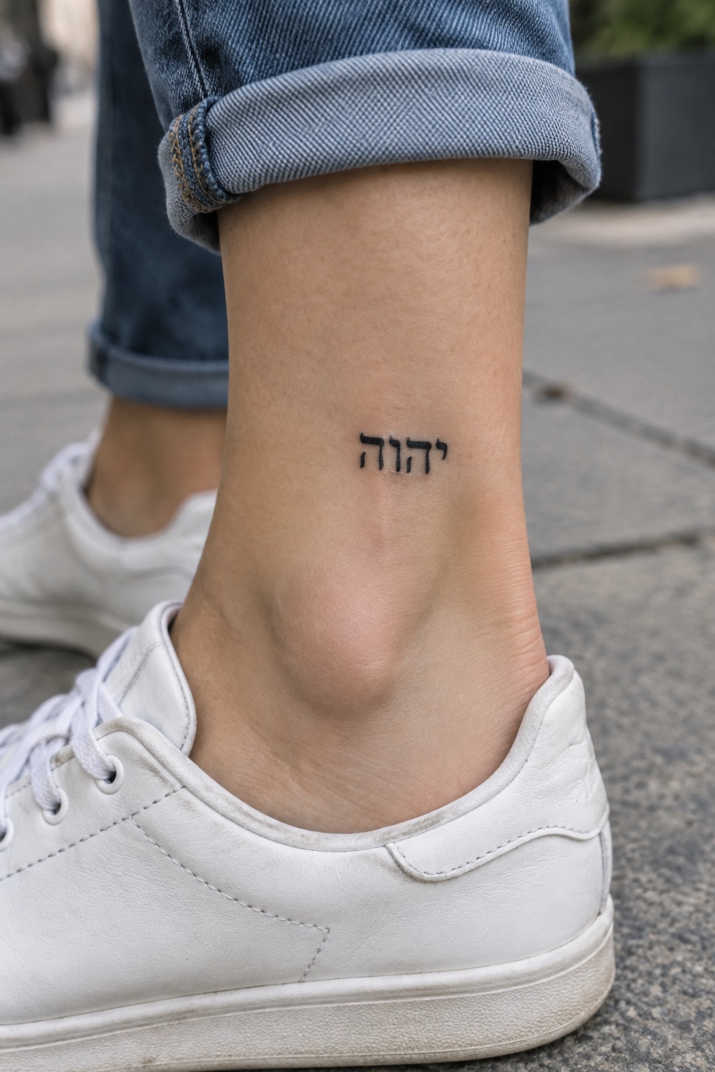 Close up of a small black Hebrew tattoo spelling YHWH on the inner ankle above a white sneaker.