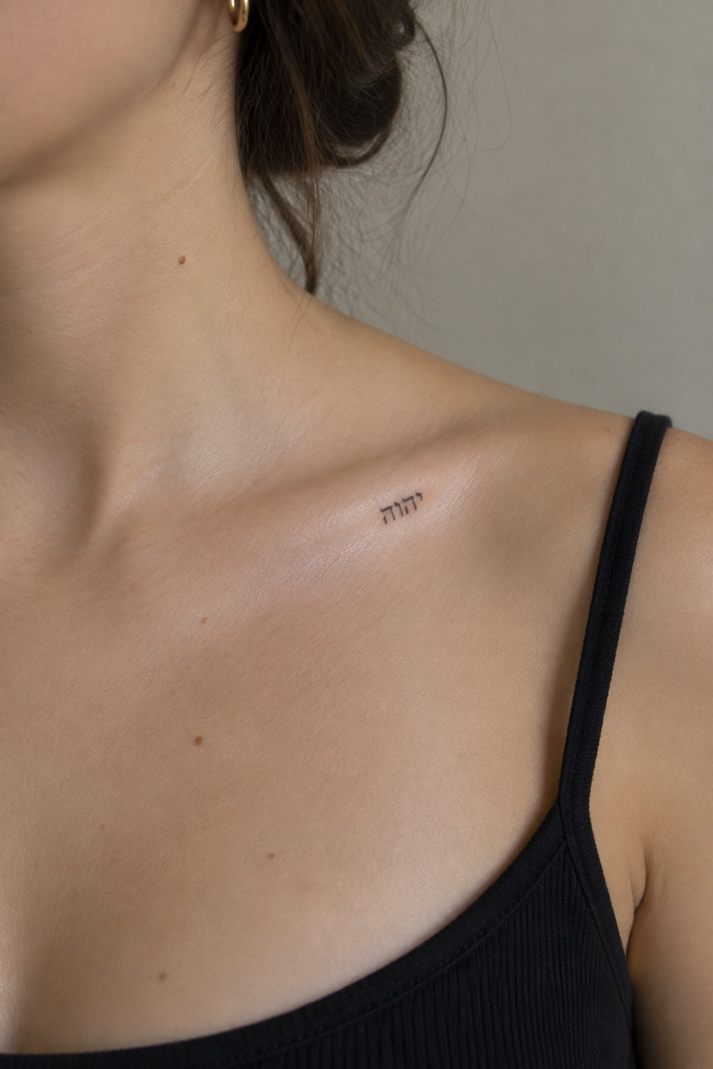Woman's collarbone with Hebrew tattoo and black spaghetti strap top on fair skin