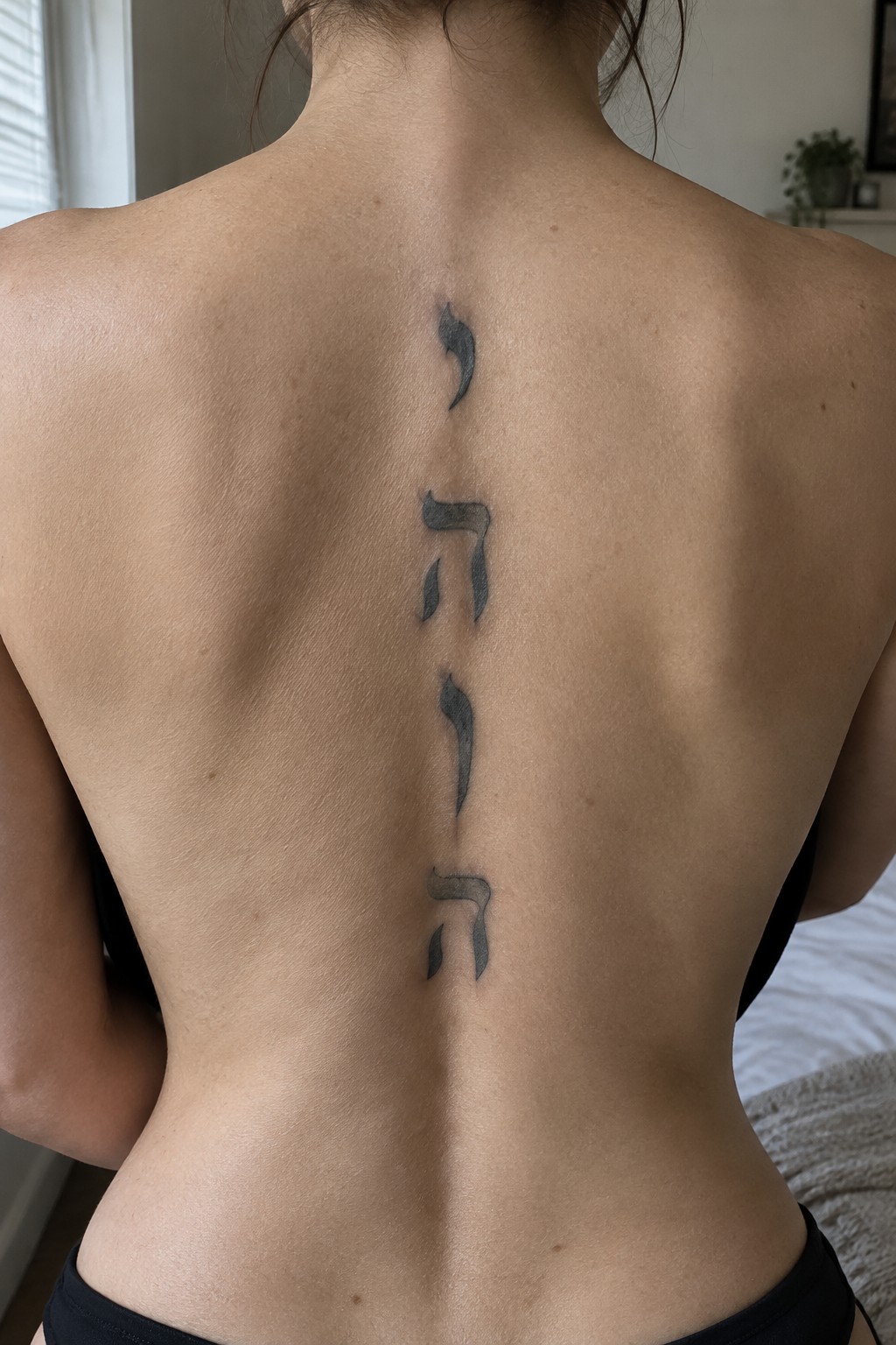 Vertical black Hebrew tattoo spelling YHWH down bare back along spine