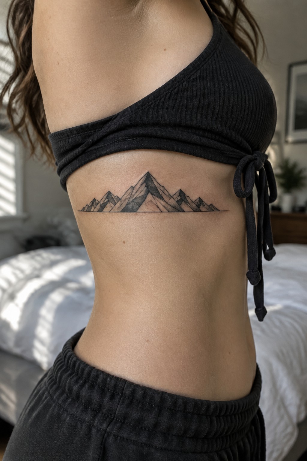 A woman with a fine-line mountain range tattoo beneath her bra on the side of her ribs.
