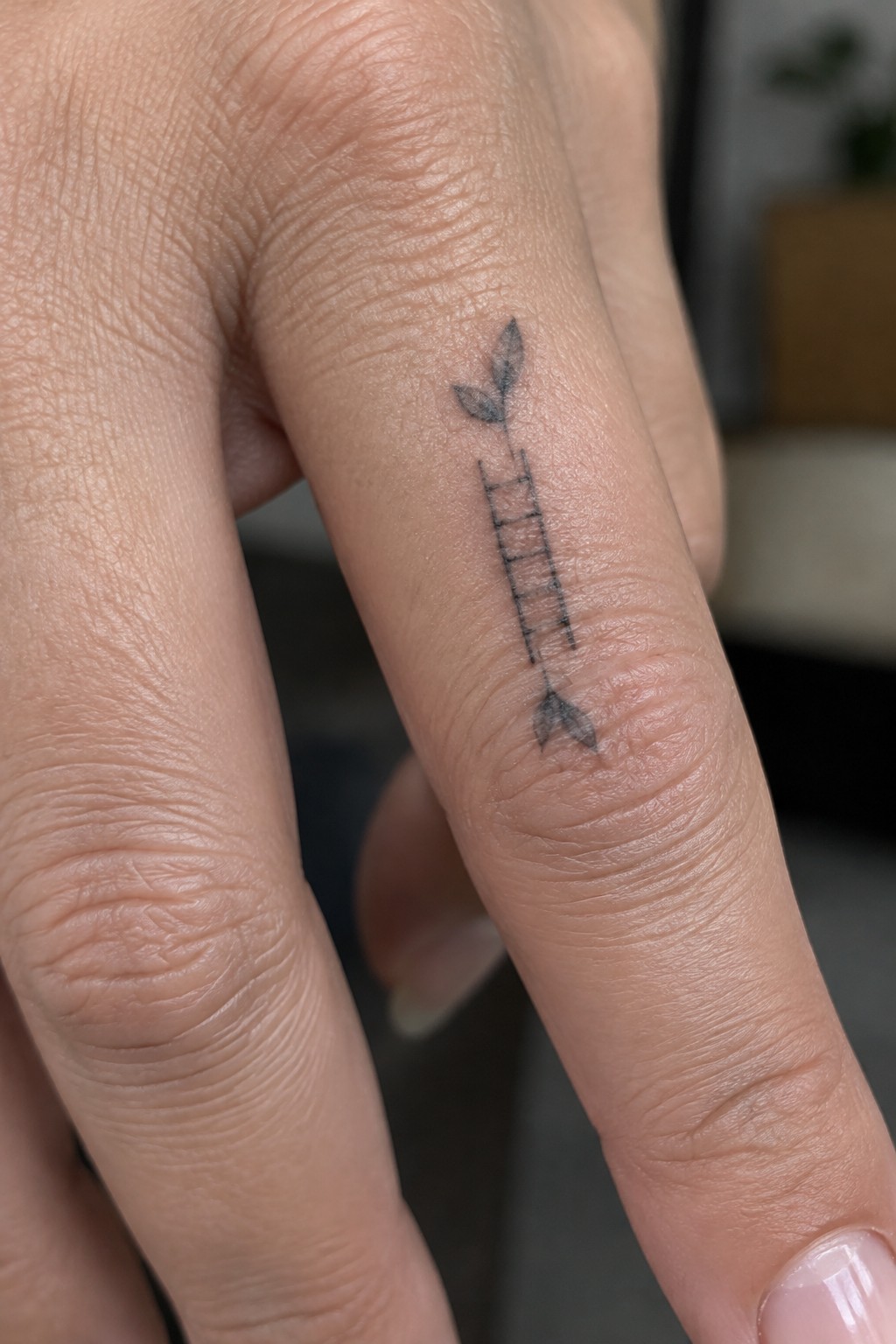 Small black ladder tattoo with leaves on a finger.